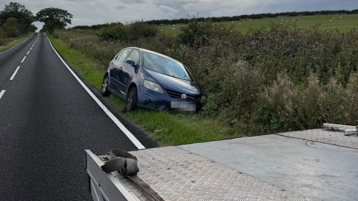 Blue hatchback that has left a country road and stopped in the grass verge, seen from the bed of the recovery truck