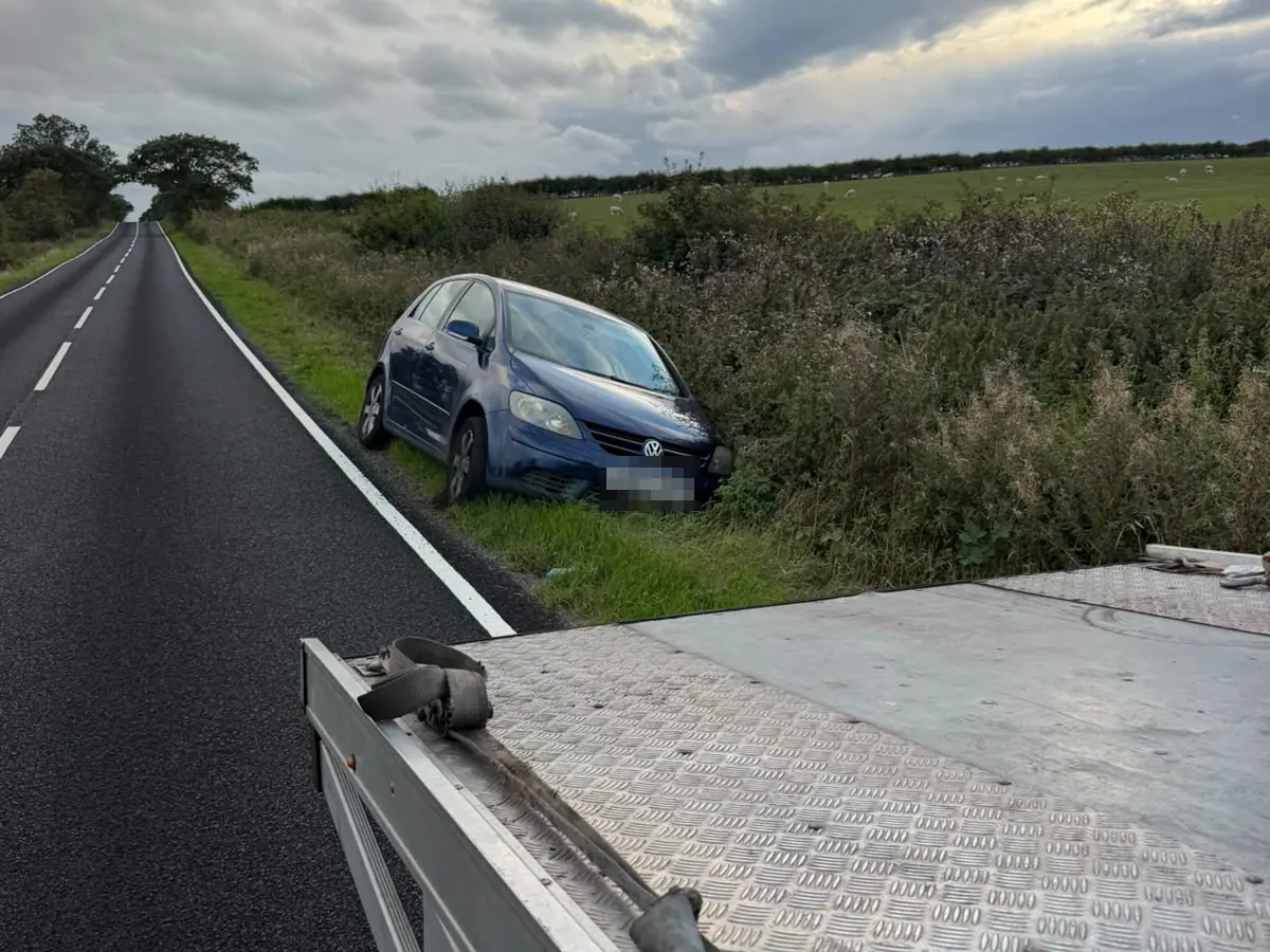 Blue hatchback that has left a country road and stopped in the grass verge, seen from the bed of the recovery truck