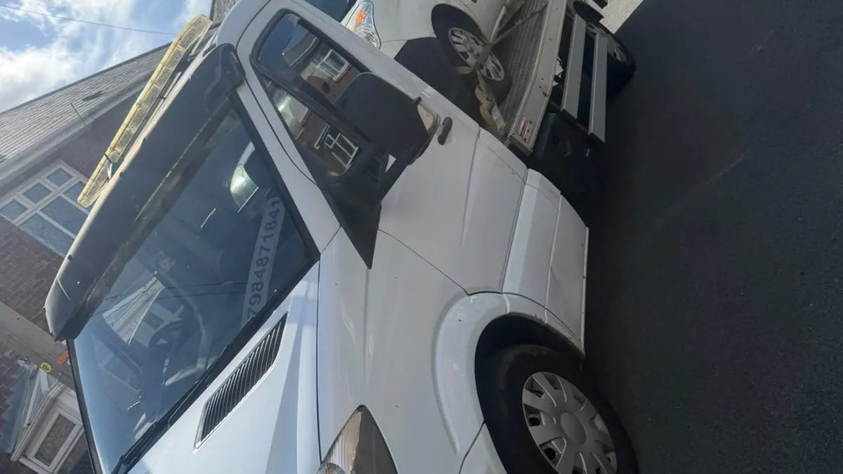 White recovery truck with a white van strapped on the back, parked on a residential street under a blue sky