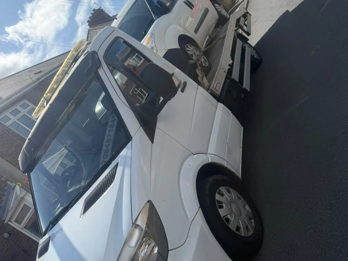 White recovery truck with a white van strapped on the back, parked on a residential street under a blue sky